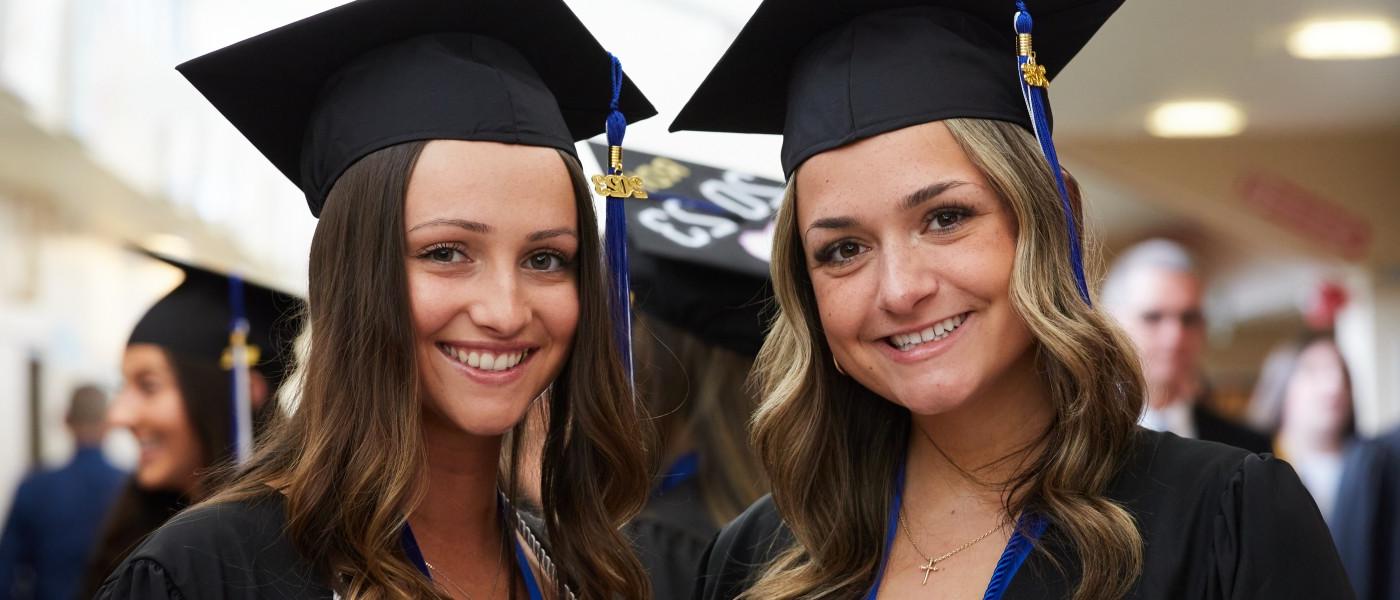 Two students wearing cap and gown pose at U N E's 2023 commencement ceremony