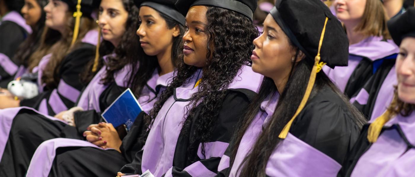 学生 wearing cap and gown sit in a row at the 2023 UNE Commencement ceremony